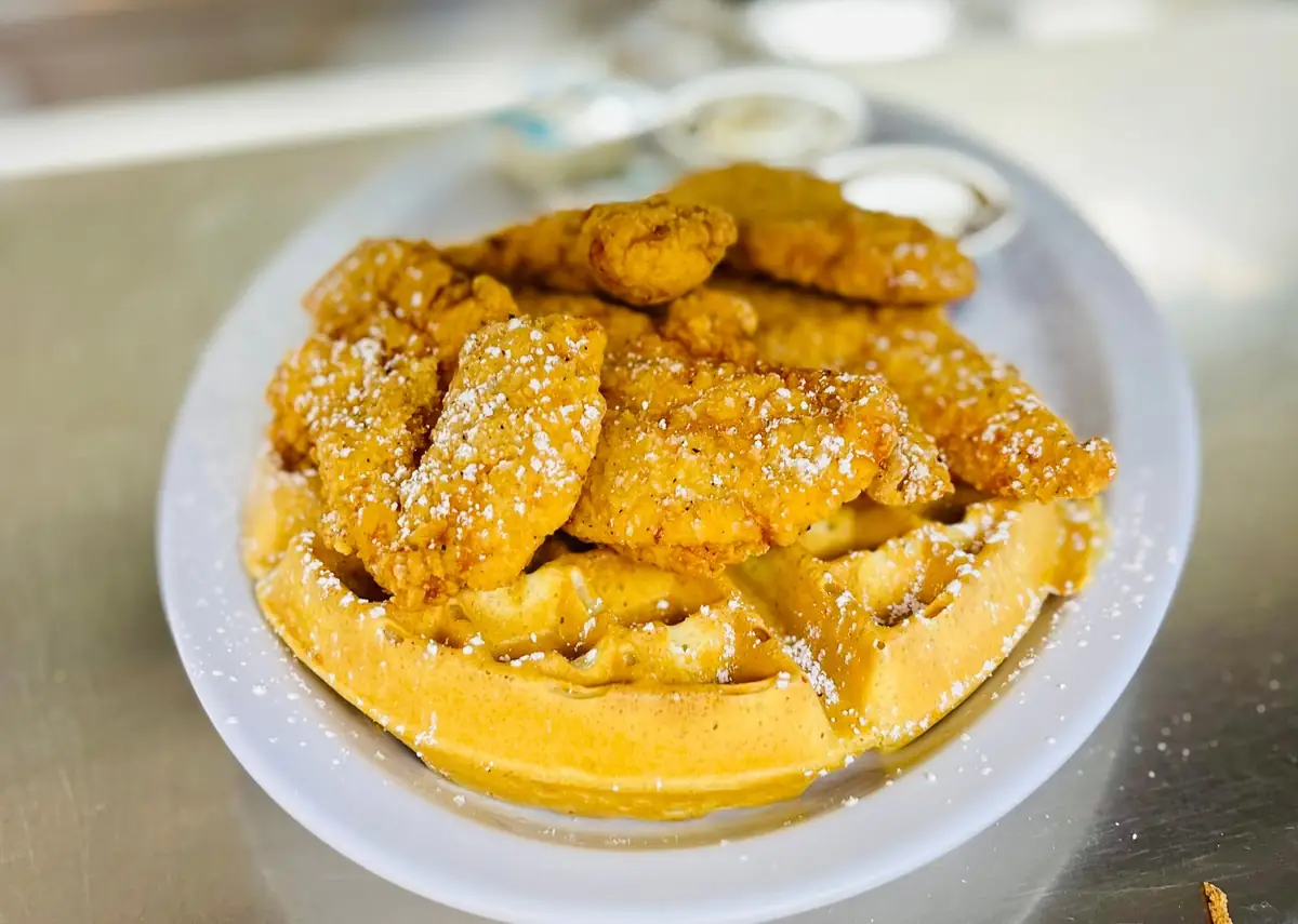 Crispy chicken tenders piled on a golden waffle and dusted with powdered sugar