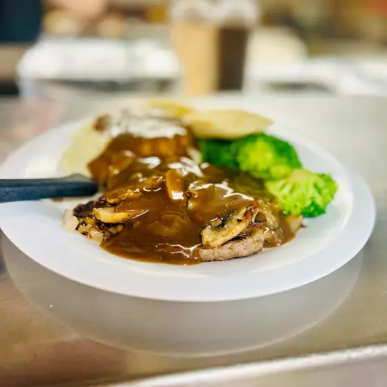 Hamburger steak smothered in mushroom and onion gravy with mashed potatoes and broccoli