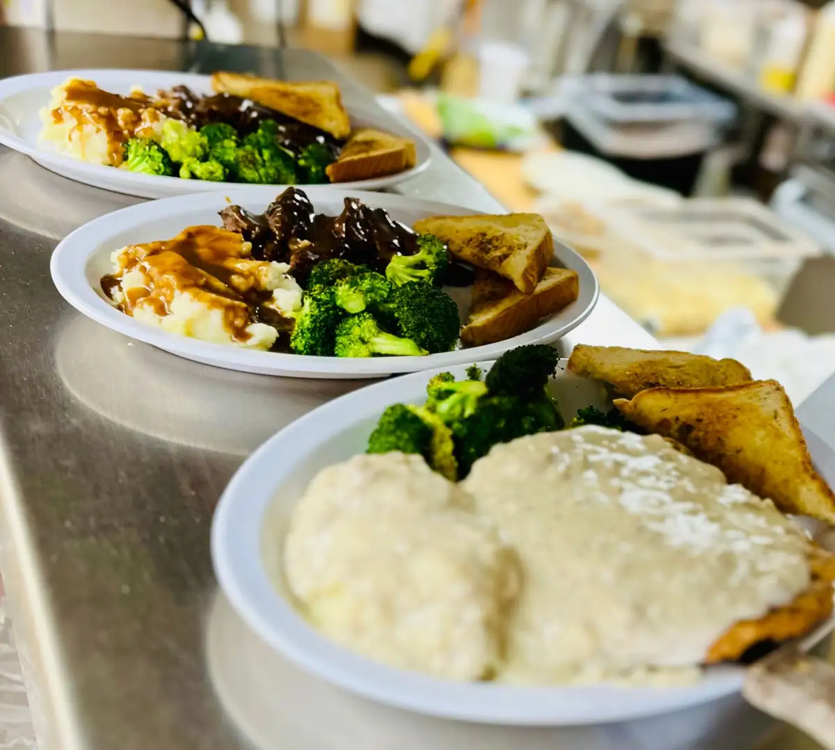 Three dinner plates lined up on the kitchen pass: beef tips with gravy, mashed potatoes, broccoli and Texas toast, with country-fried steak and gravy in front