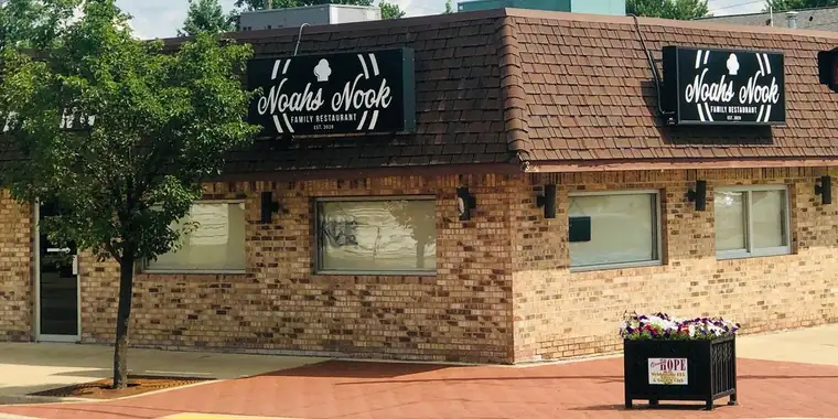 The restaurant's brick corner building with two black Noah's Nook Family Restaurant signs on the roofline and a flower planter on the sidewalk